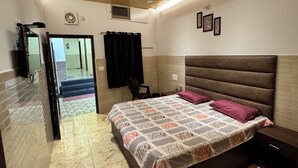 A bedroom with a bed, a ceiling fan, a mirror, and a door leading to a hallway. - Hotel Utsav (Khatima)