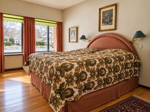 Una camera da letto con un letto grande, una finestra con tende, un termosifone e due lampade a parete.