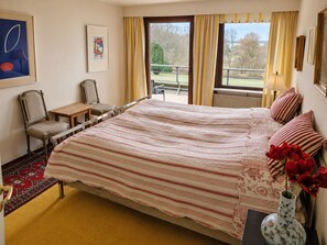 Una camera d'albergo con un letto, una sedia, un tavolino, un vaso con fiori e vista sull'esterno.