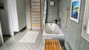 A modern bathroom with a bathtub, shower, and a wooden ladder.