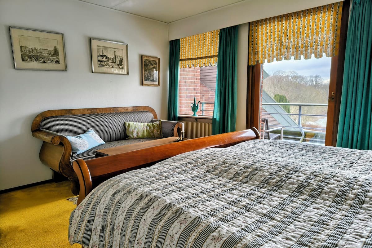 Un dormitorio con una cama grande, un banco de madera, un sofá y dos cuadros en la pared.