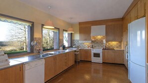 Une cuisine moderne avec des meubles en bois, un réfrigérateur blanc et une grande fenêtre donnant sur la forêt.