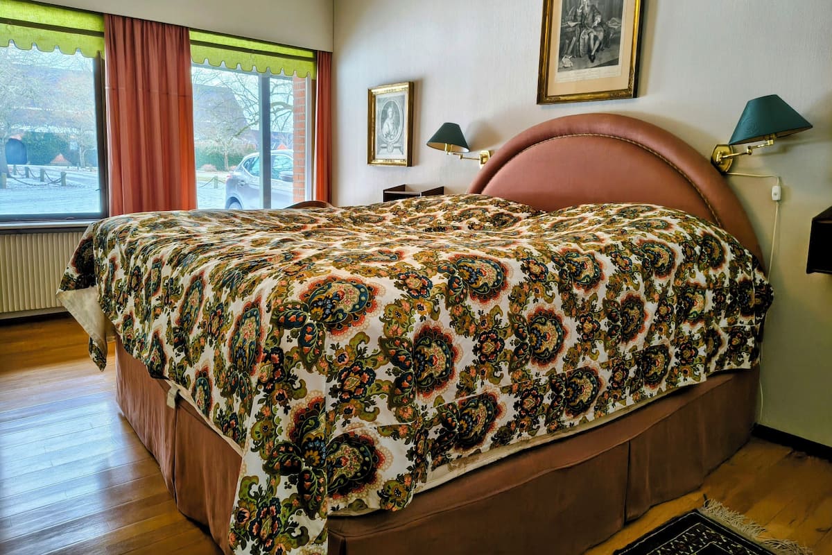 Un dormitorio con una cama grande, una ventana con cortinas, un cuadro en la pared y una lámpara en la mesita de noche.