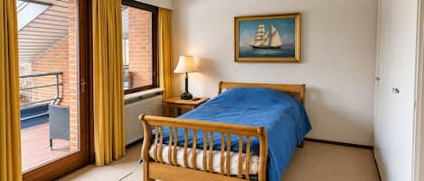 A bedroom with a wooden bed, a painting of a sailboat, a window with curtains, and a radiator.