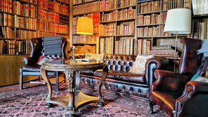 Une bibliothèque dotée de fauteuils en cuir, d’une table ronde et d’une vaste collection d’étagères remplies de livres.