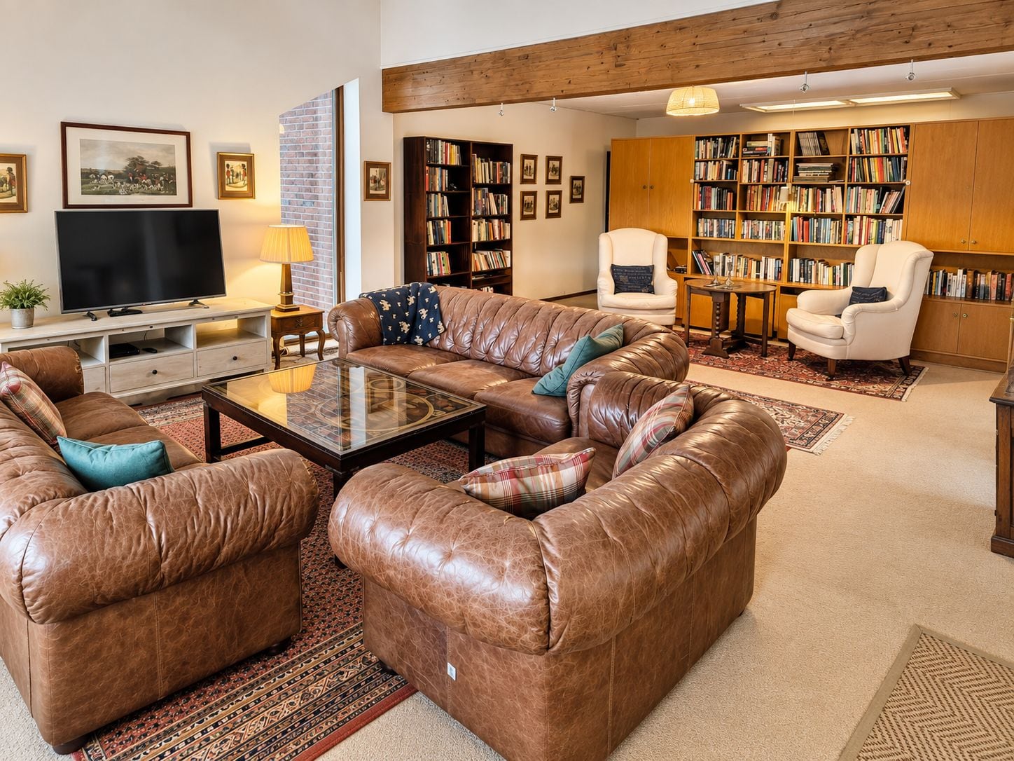 Una sala de estar con sofás de cuero, una mesa de centro, televisor, estanterías y chimenea.
