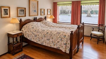 Une chambre à coucher avec un lit en bois, une table de chevet, une lampe, une chaise et une fenêtre avec des rideaux.