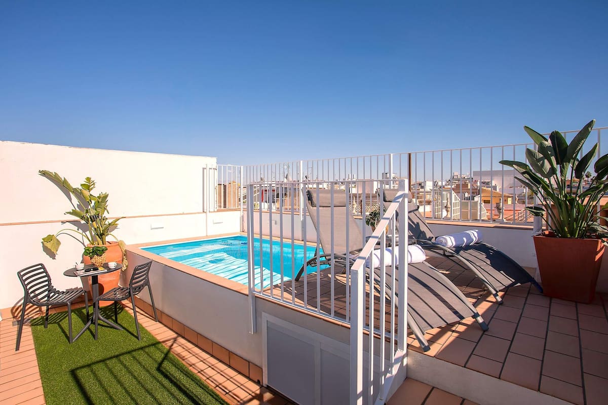 Zona de piscina al terrat amb una piscina tancada, dues cadires, una taula petita i plantes en testos.