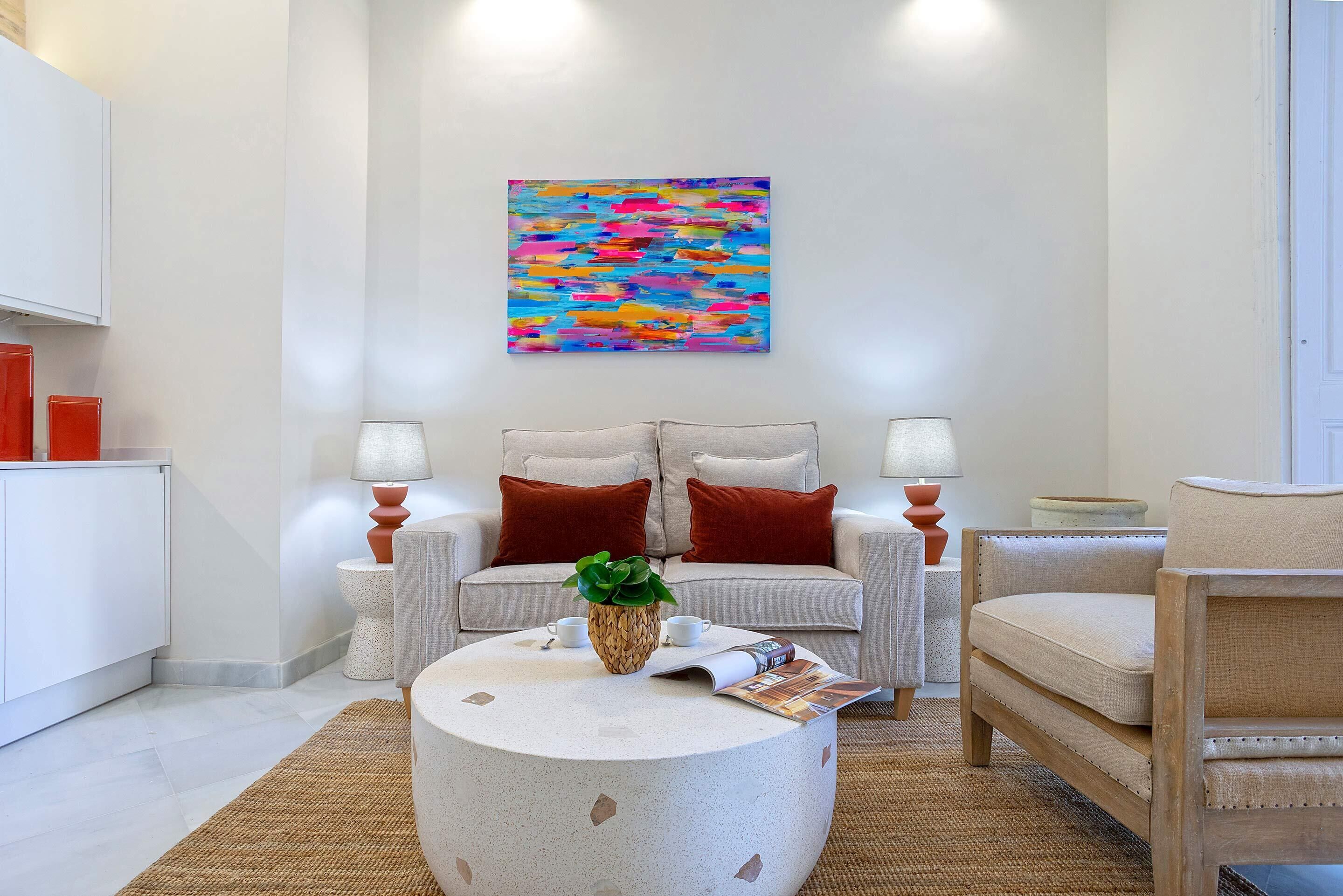 A modern living room with a sofa, armchairs, a coffee table, and a colorful abstract painting on the wall.