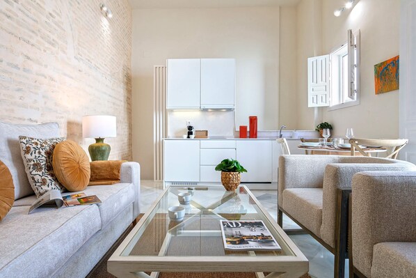 A modern living room with a sofa, a glass coffee table, and a kitchen in the background. - Genteel Home Mendoza Ríos (Seville)