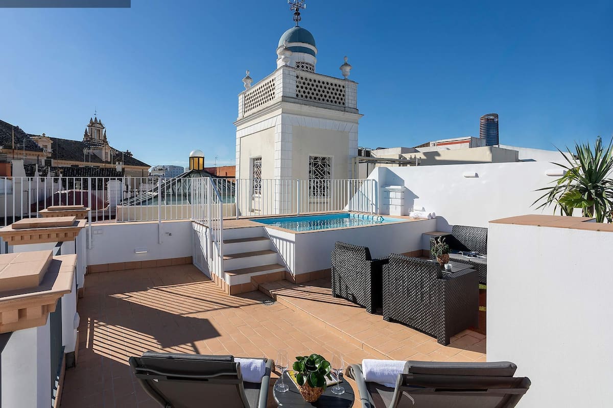 Una terrassa al terrat amb una piscina, seients a l'aire lliure i un edifici blanc amb cúpula.