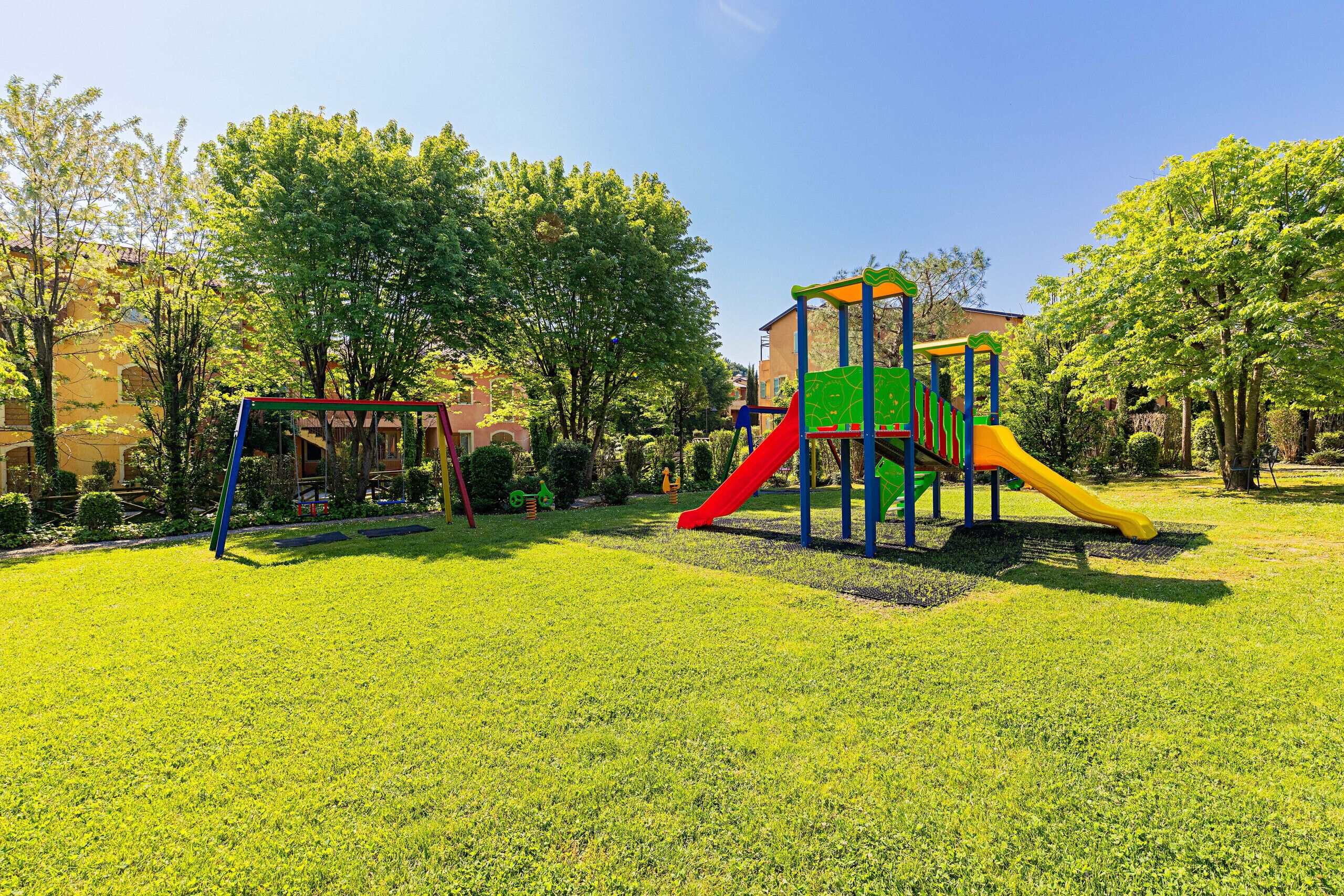 Ein Spielplatz mit Rutsche und Klettergerüsten in einem Park mit Gras und Bäumen.