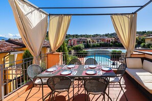 A terrace with a table set for dining, overlooking a swimming pool and a residential area. - 2 Bedroom apartment in resort with pools (Manerba del Garda)