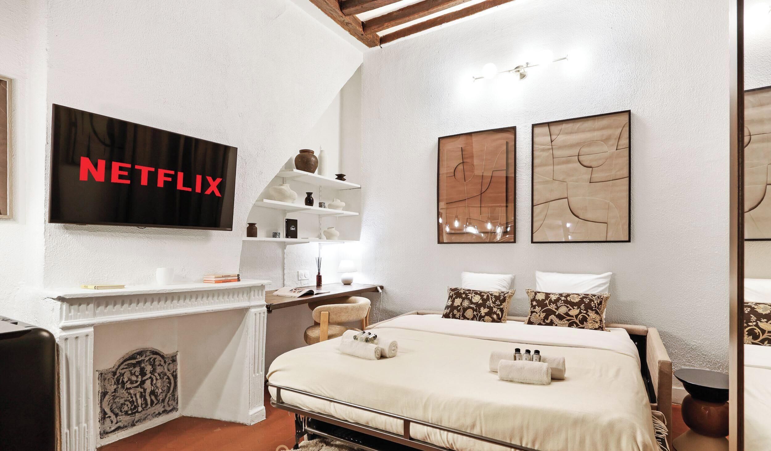 A modern bedroom with a bed, bedside tables, a TV mounted on the wall, and artwork on the walls.