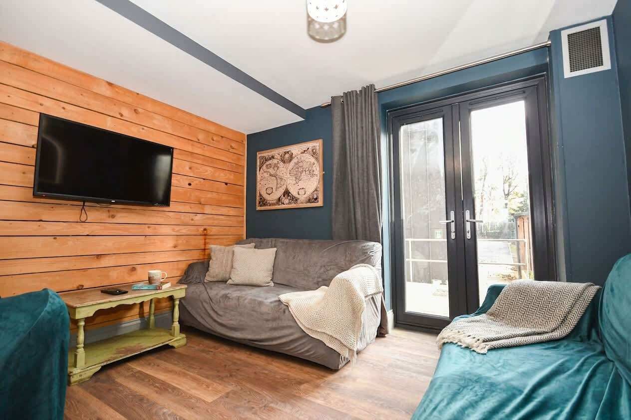 A cozy living room with a flat-screen TV mounted on a wooden wall, a grey sofa, and a small wooden table with a mug.