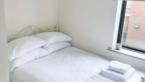 Yhden hengen sänky valkoisilla lakanoiden ja tyynyjen kanssa, ikkuna, jossa on sälekaihdin, ja patteri.