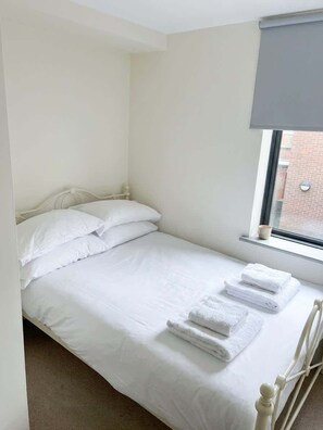 A single bed with white bedding and pillows, a window with a blind, and a radiator. - Budget 5BR Apartment in the Heart of Headingley (Headingley)