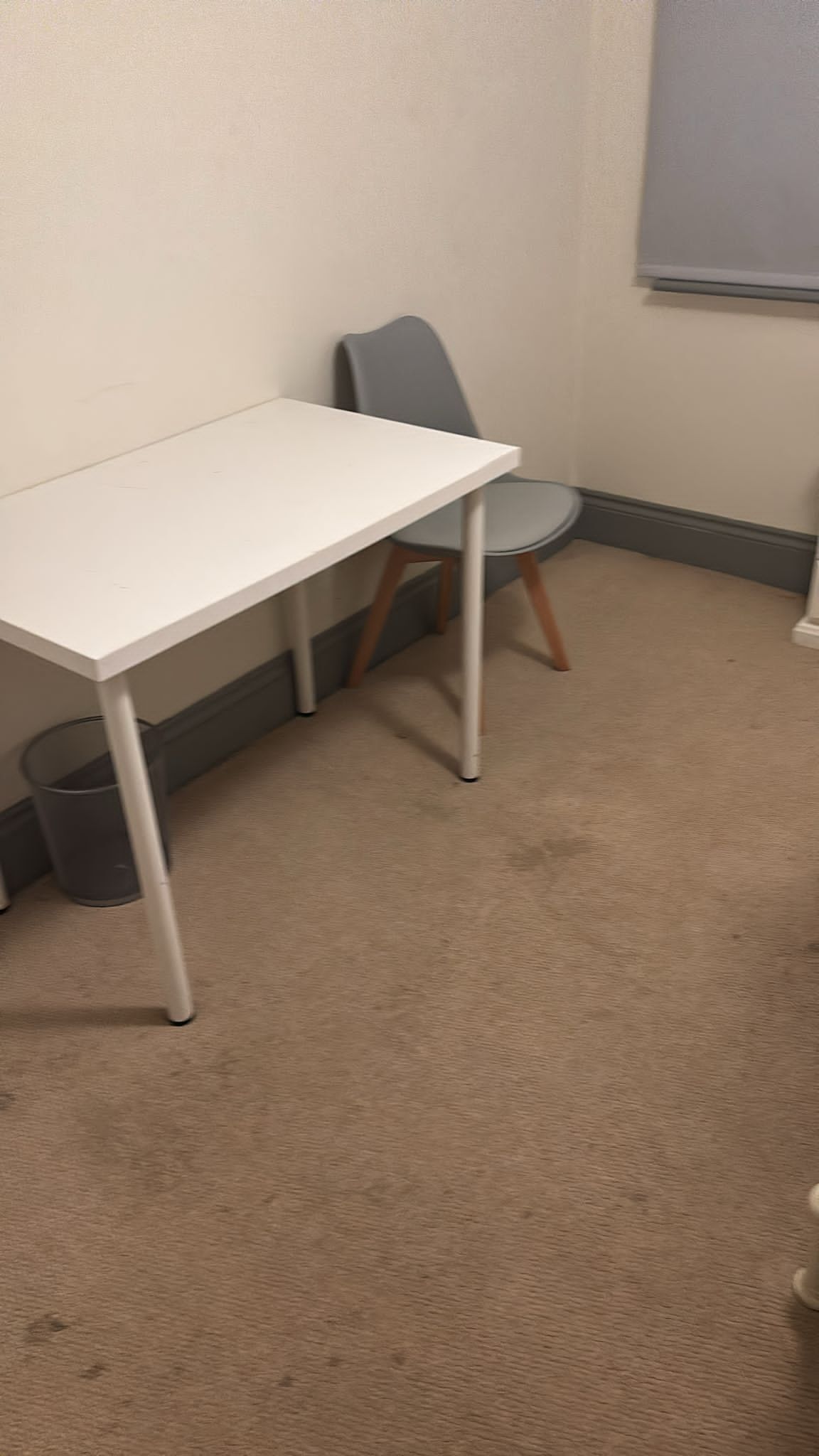 A white table with metal legs, a grey chair, and a carpeted floor.
