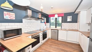 A modern kitchen with white cabinets, a wooden countertop, a built-in microwave, and a stainless steel dishwasher. - Convenient 4BED Budget Apartment in Headingley (Headingley)