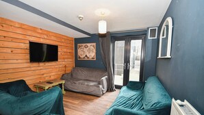 A room with a wooden wall, a flat-screen TV, a sofa, a chair, and a window with curtains. - Convenient 4BED Budget Apartment in Headingley (Headingley)