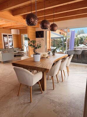 A modern dining area with a wooden table, white upholstered chairs, and hanging spherical light fixtures. - Mountain chalet overlooking Cordon near Combloux, Megeve and Chamonix (Sallanches)