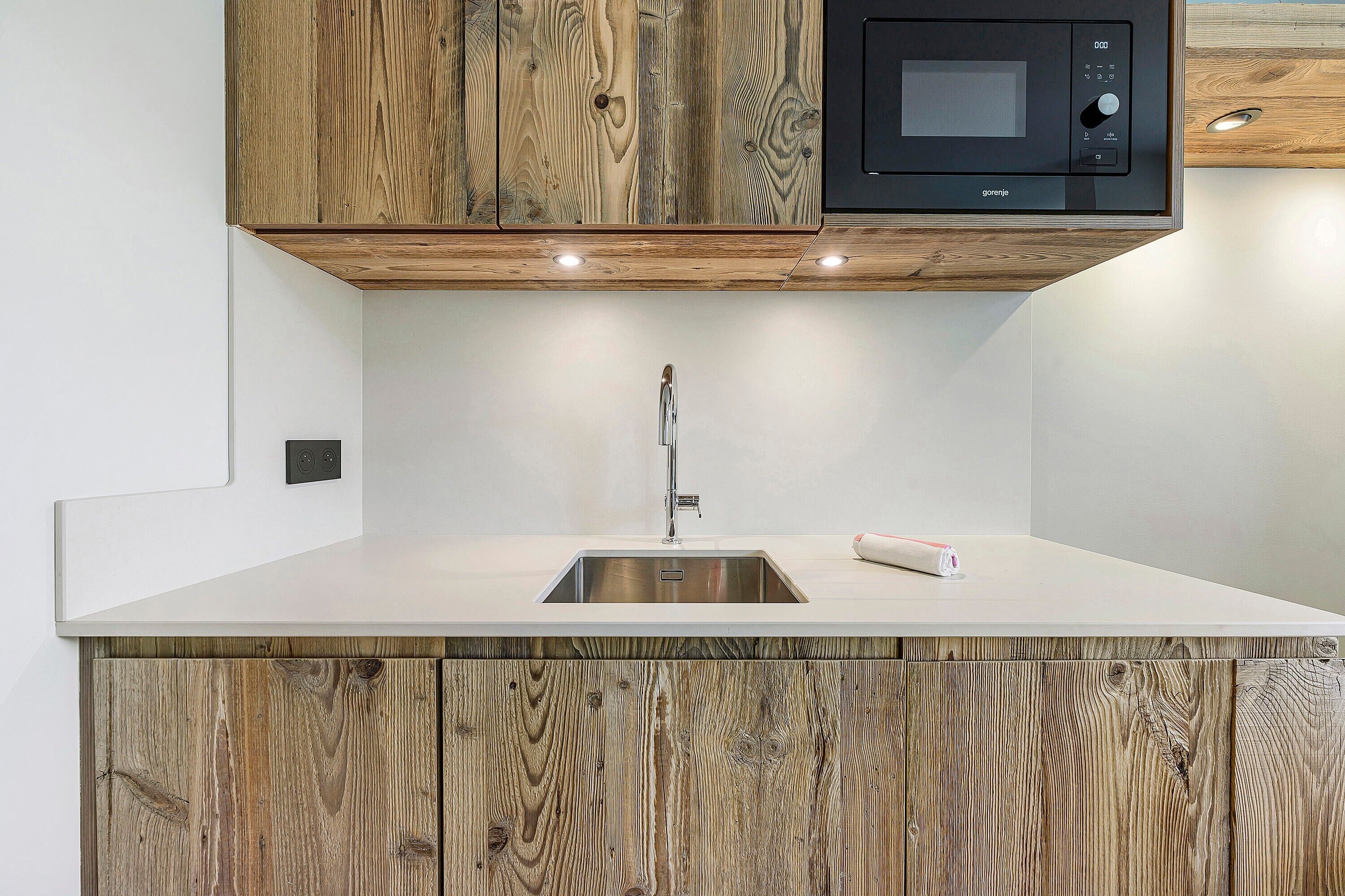 A kitchen with a wooden cabinet, a microwave, and a stainless steel sink.