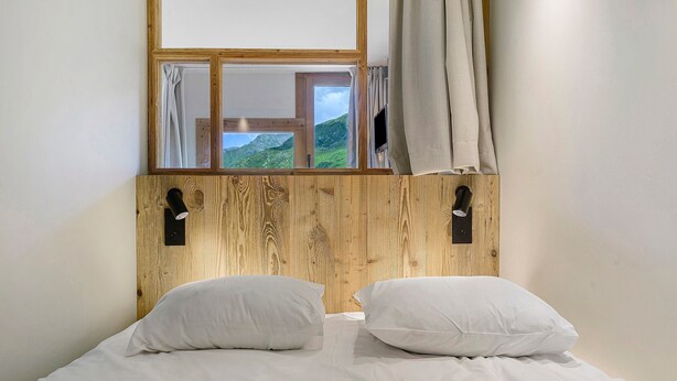 Ein Bett mit weißer Bettwäsche, einem Holz-Kopfteil und einem Fenster mit Vorhängen.
