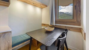 Ein kleiner Raum mit einem Holztisch, einer Bank, einem Fenster mit Bergblick und einer Deckenleuchte.