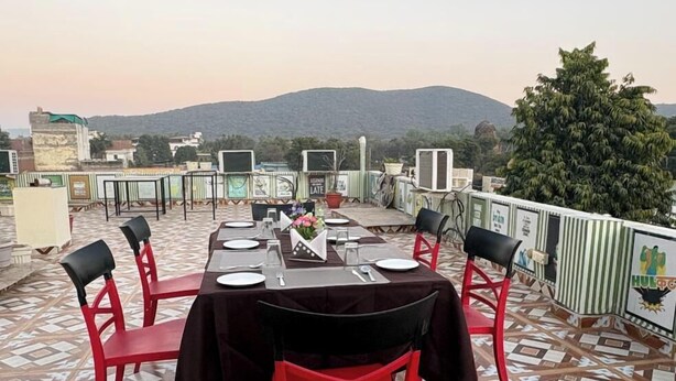 A dining area with a table set for four, surrounded by red chairs, on a patterned floor with a view of hills in the background. - Hotel Tiger Homestay (Sawai Madhopur)