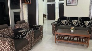 A spacious living room with two patterned sofas, a wooden coffee table, and a ceiling fan. - Hotel Tiger Homestay (Sawai Madhopur)