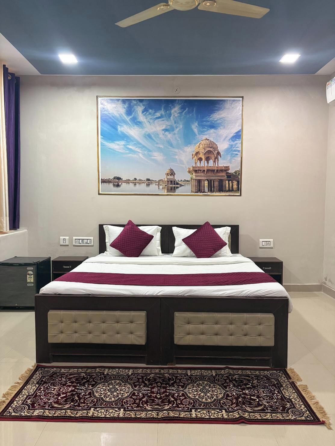 A bedroom with a bed, a nightstand, a dresser, a ceiling fan, and a large framed picture on the wall.