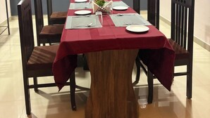 A dining area with a long wooden table covered by a red tablecloth, surrounded by dark wooden chairs. - Hotel Tiger Homestay (Sawai Madhopur)