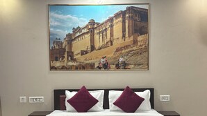 A hotel room with a large bed, two nightstands, a wall-mounted painting of a historical building, and a patterned rug. - Hotel Tiger Homestay (Sawai Madhopur)