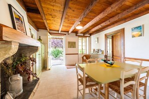 A dining area with a wooden table and chairs, a fireplace, and a view of the outdoors. - Gîte la Sarpette – Secluded Retreat in Nature (Sainte-Radegonde)