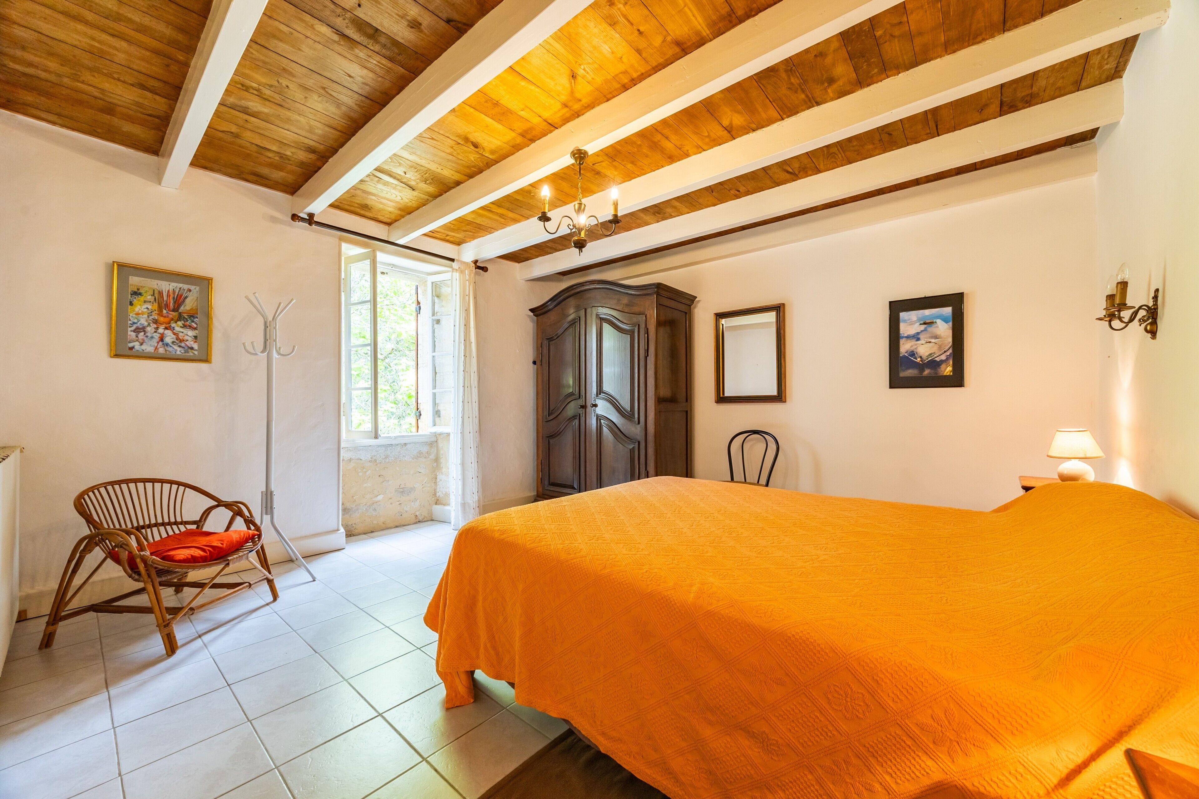 A room with a bed, a wooden ceiling, a chair, a wardrobe, and a painting on the wall.