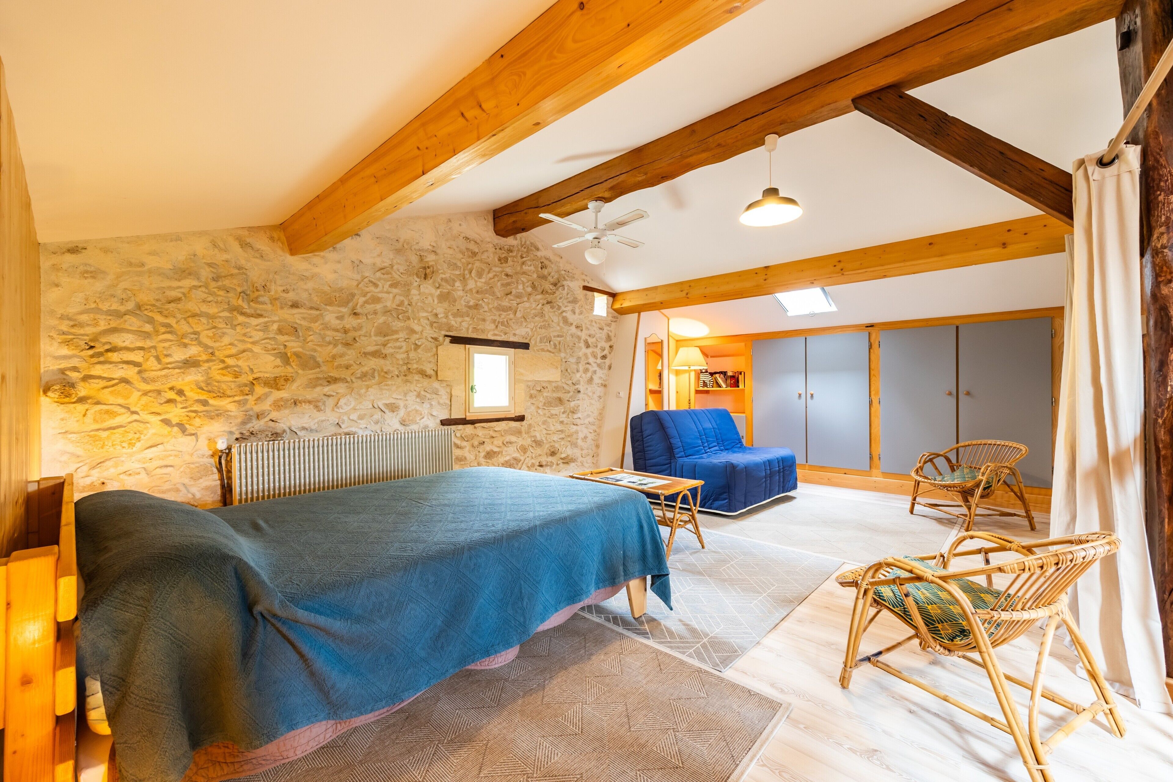 Un dormitorio con pared de piedra, vigas de madera, cama, silla y armario.