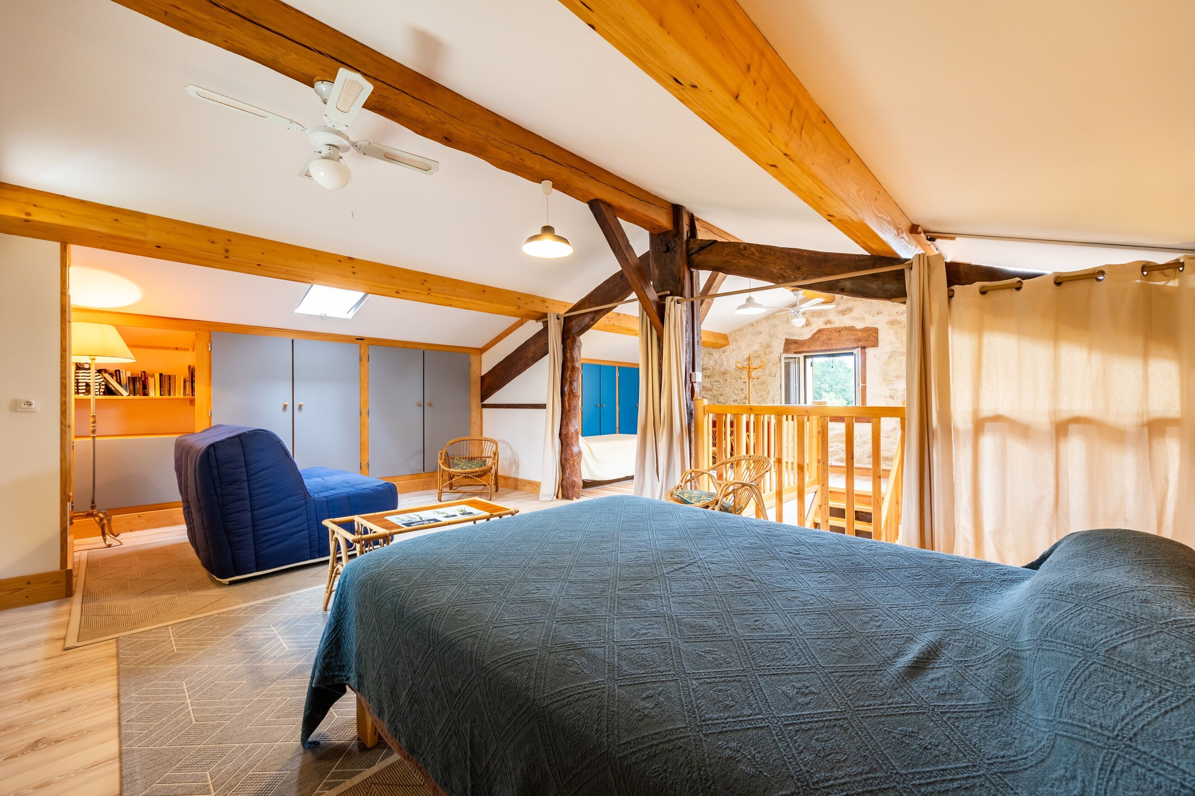 Ein Zimmer mit einem Bett, einem Schreibtisch, einem Stuhl, einem Fenster und einer Holzbalkendecke.