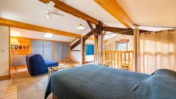Ein Zimmer mit einem Bett, einem Schreibtisch, einem Stuhl, einem Fenster und einer Holzbalkendecke.