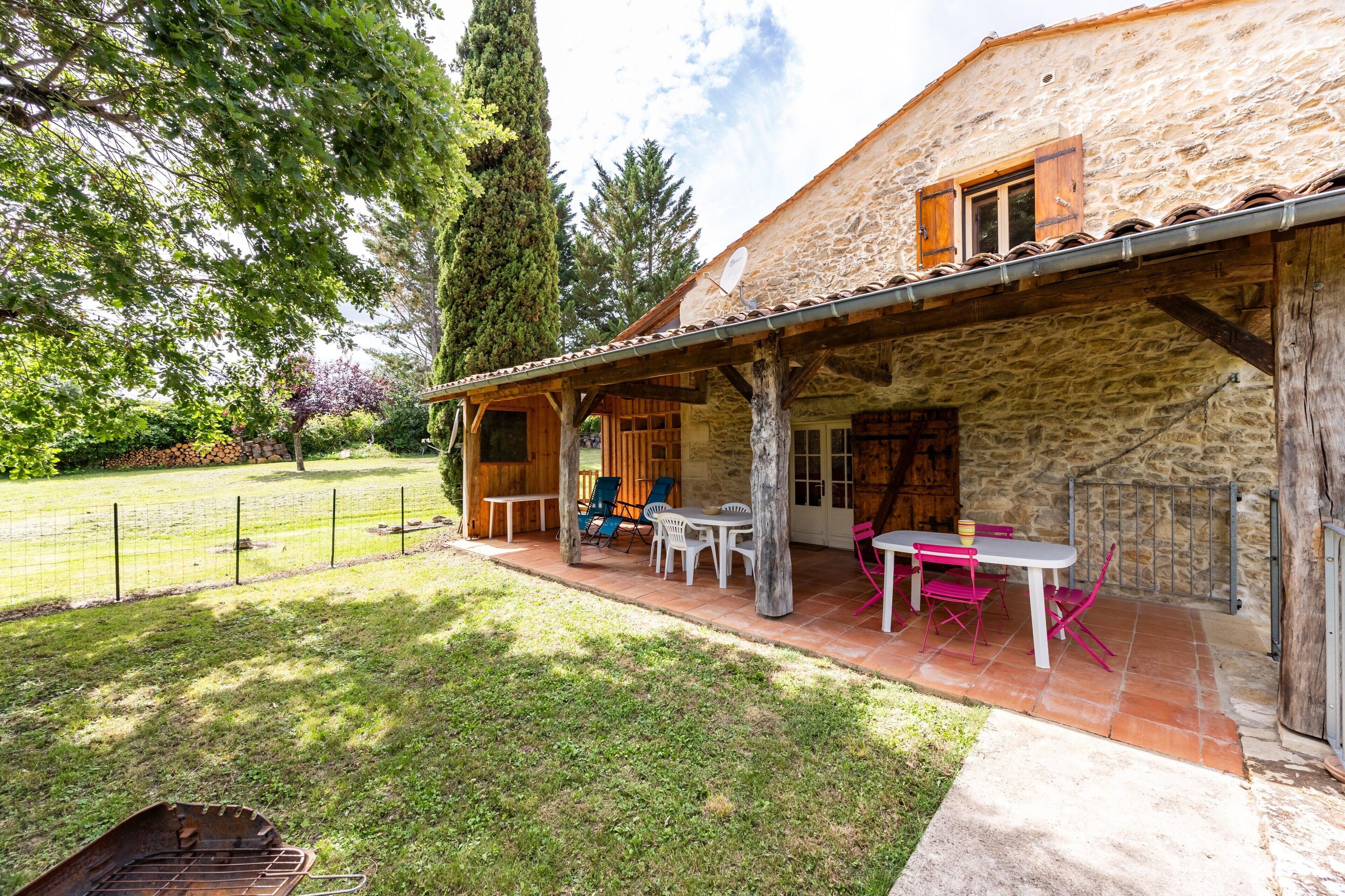 Ein Steinhaus mit überdachter Terrasse, Sitzgelegenheiten im Freien und einem umzäunten Garten.
