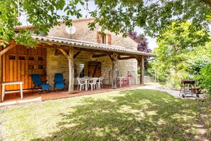 A stone house with a covered patio, outdoor seating, and a garden. - Gîte la Sarpette – Secluded Retreat in Nature (Sainte-Radegonde)