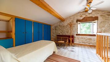 Un dormitorio con cama, armario azul, paredes de piedra, techo de madera y ventana.
