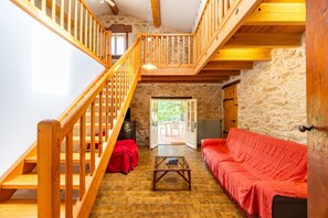 A rustic interior with a wooden staircase, a red sofa, and a stone wall. - Gîte la Sarpette – Secluded Retreat in Nature (Sainte-Radegonde)