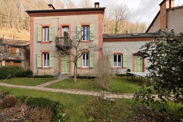 Un bâtiment à deux étages, doté de volets verts, d’une façade en pierre et d’un petit jardin agrémenté d’un sentier.