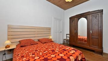 A bedroom with a wooden headboard, a large bed with a polka dot blanket, a wooden wardrobe, and a mirror.