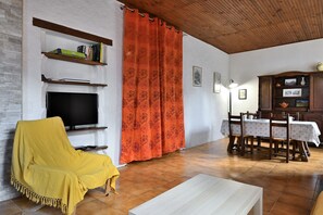 Un salon avec un téléviseur, un fauteuil jaune, une table à manger avec des chaises et un buffet en bois.