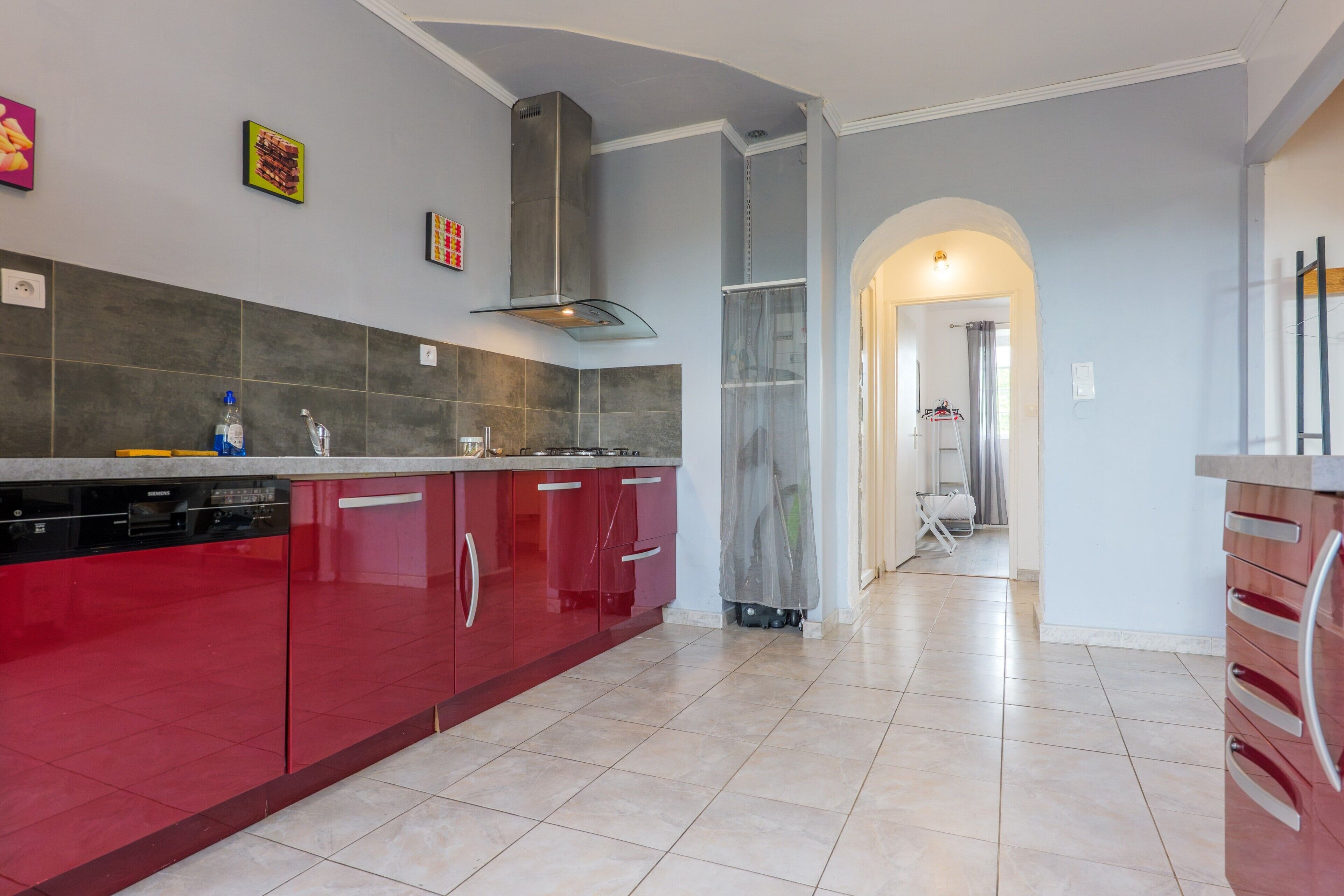 Une cuisine moderne avec des armoires rouges, une hotte de cuisinière en acier inoxydable et un dosseret carrelé.