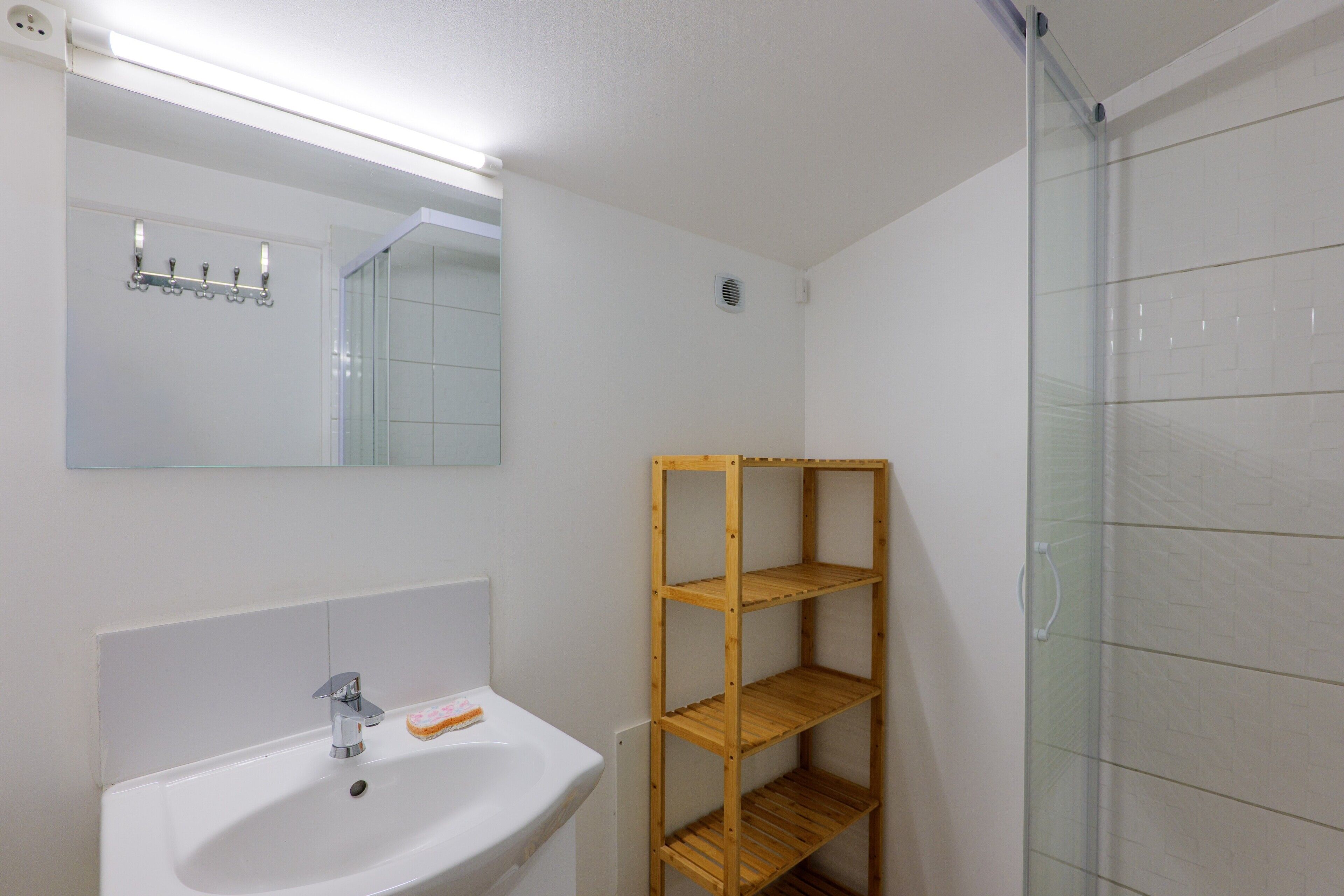 Un bagno con lavandino bianco, specchio e mensole di legno.