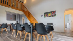 A dining area with a staircase, black chairs, and a parrot painting on the wall. - Les Traverses Gîte with Shared Pool, Wi-Fi, and Air Conditioning (Chauzon)