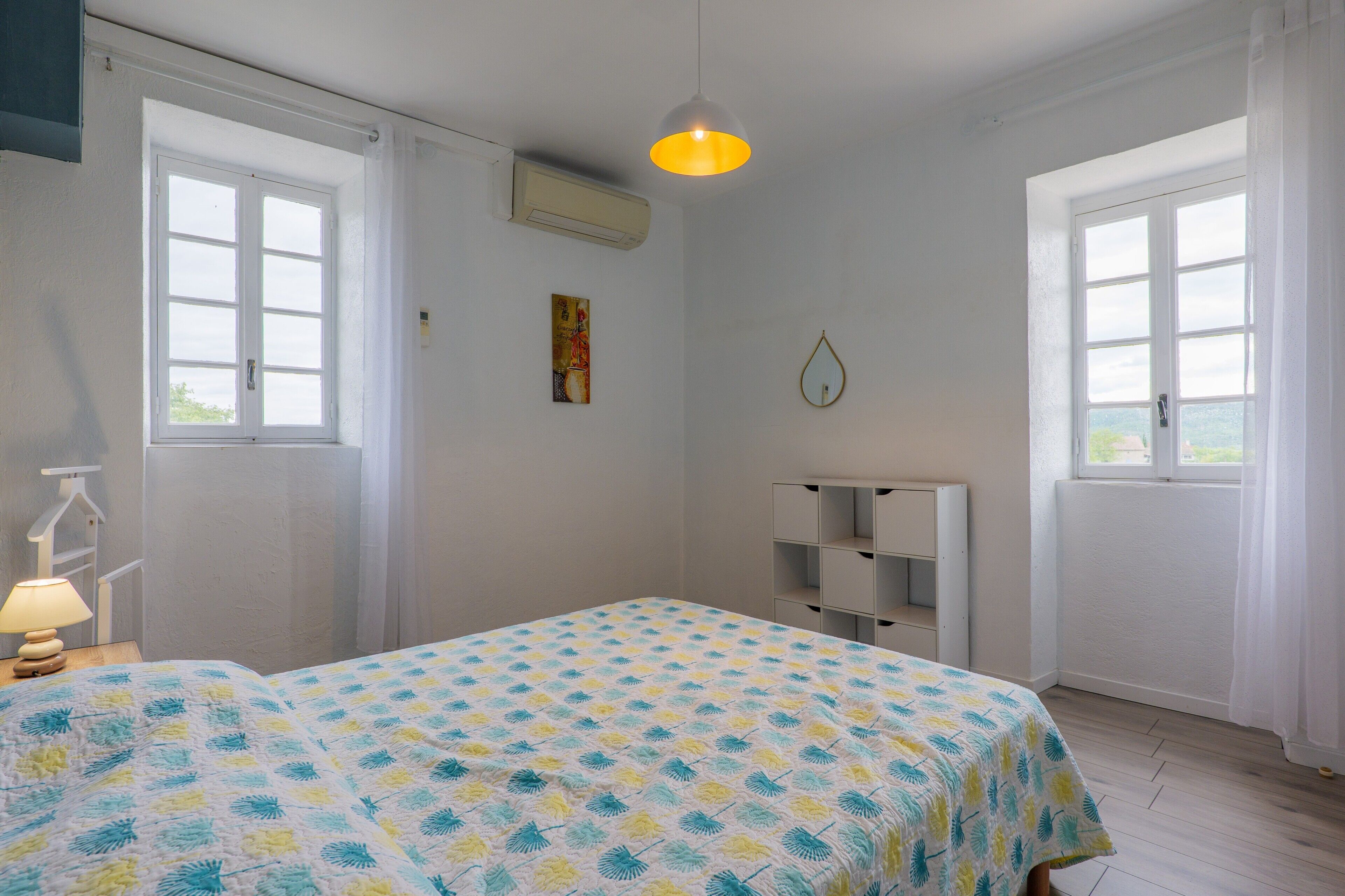 A room with a bed, a bedside lamp, a wall-mounted air conditioner, and a window with a view.