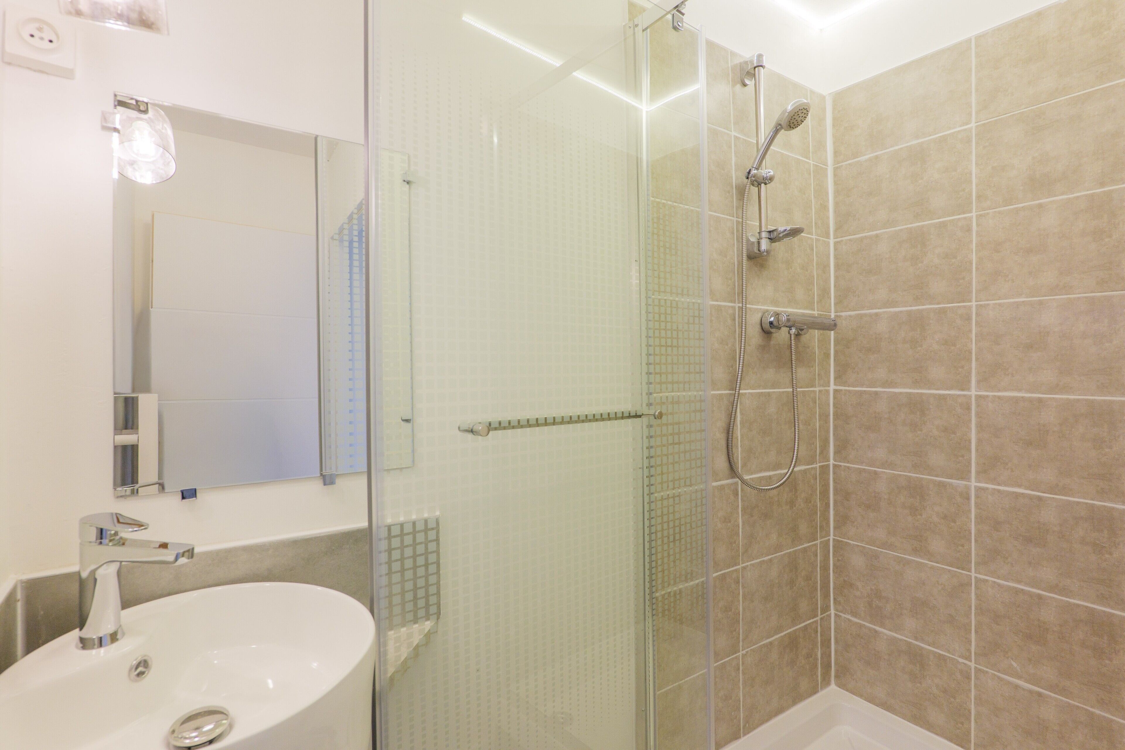 Un baño con ducha de vidrio, lavamanos y espejo.